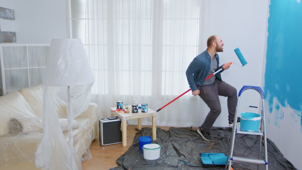 Homem animado pintando sozinho uma parede de azul e segurando um rolo de pintura.